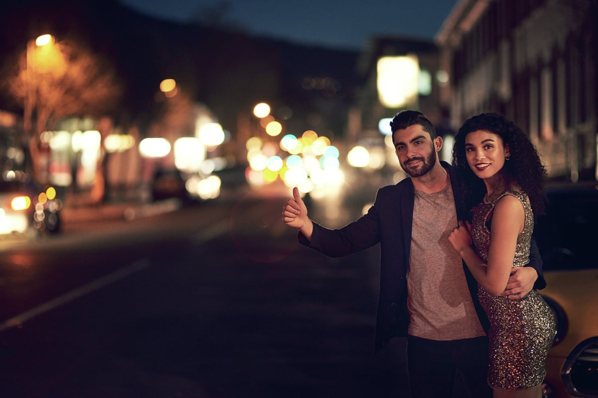 Shot of a cheerful young couple holding each other while waiting for a taxi outside in the streets at night