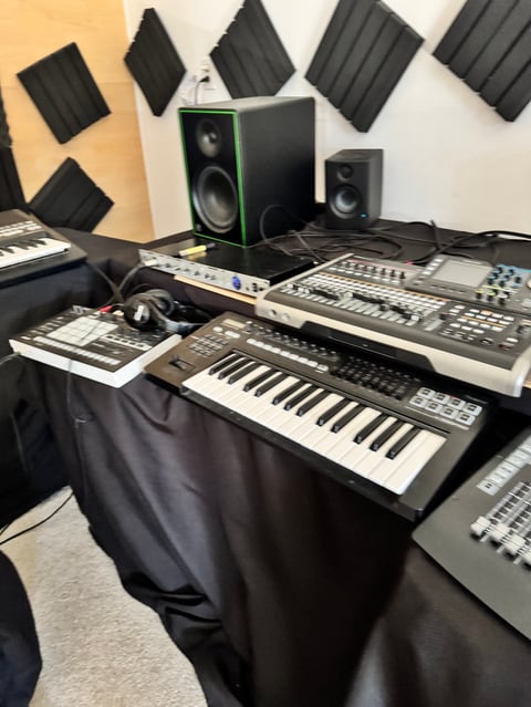 Music production setup with keyboards, synthesizers, speakers, and acoustic foam panels on walls