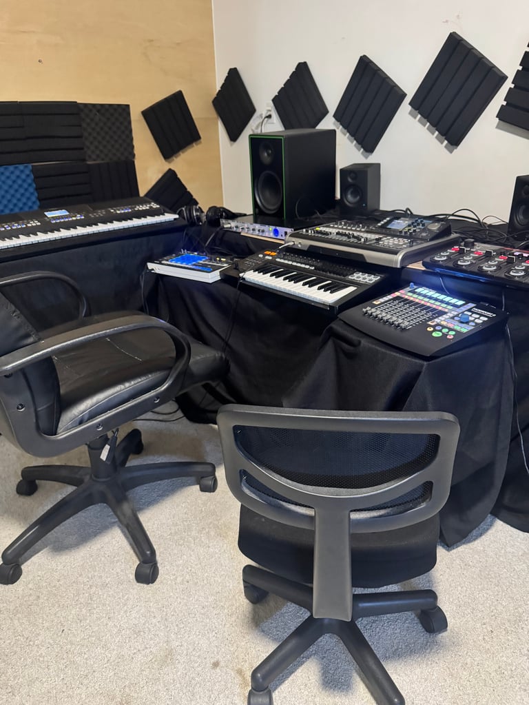 Professional music production studio setup with keyboards, mixing board, monitors, and acoustic foam panels on walls