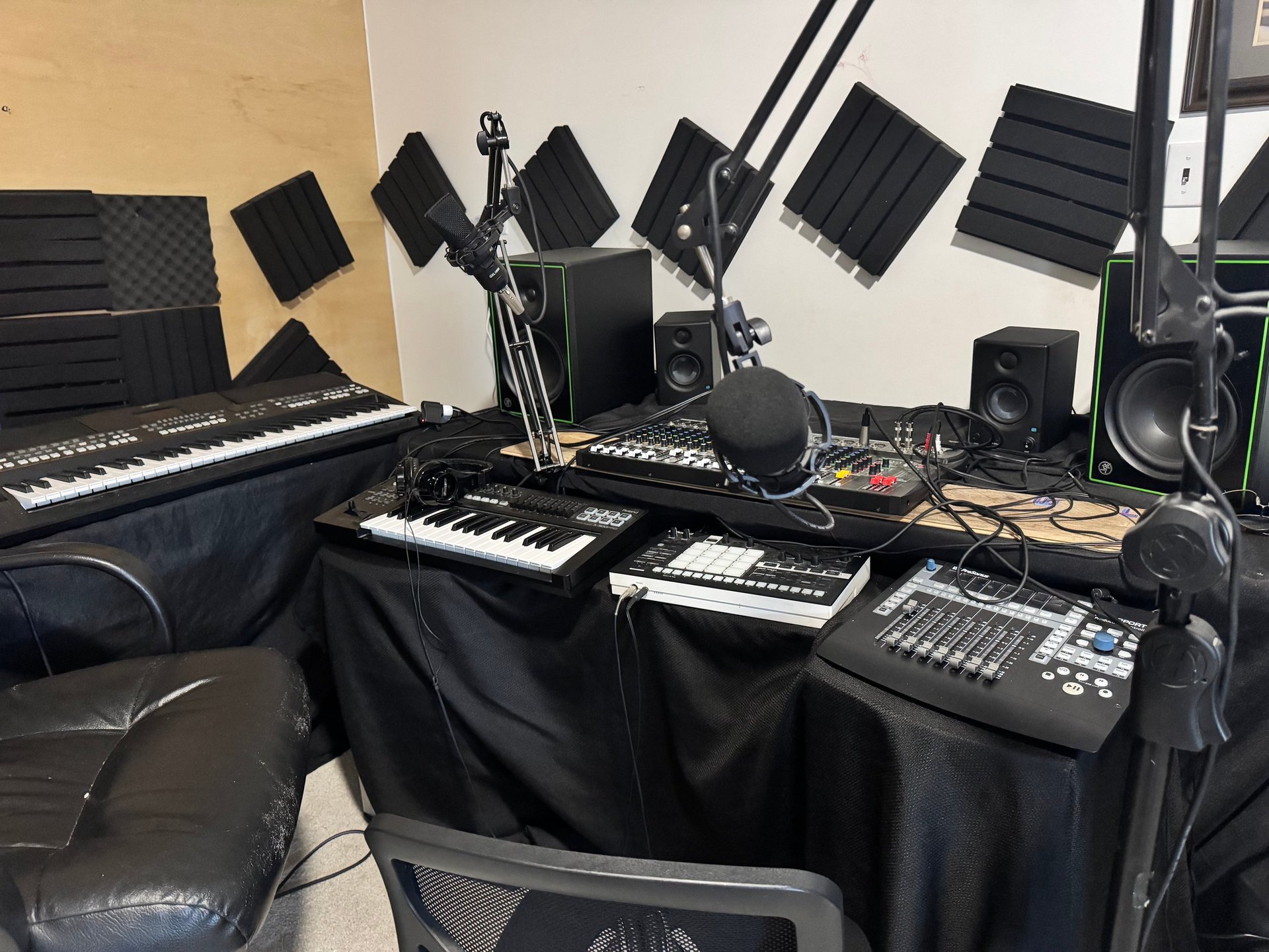 Professional music production studio setup with keyboards, audio monitors, mixing equipment, and acoustic panels mounted on walls